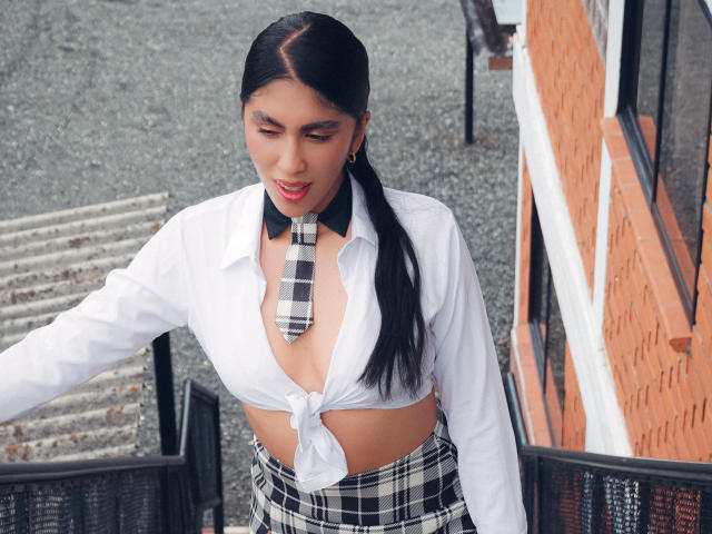 LilyGreay with black hair in a ponytail, wearing a tied-up white shirt revealing her tits, black-and-white plaid necktie, and matching skirt, looking down with a subtle smile.