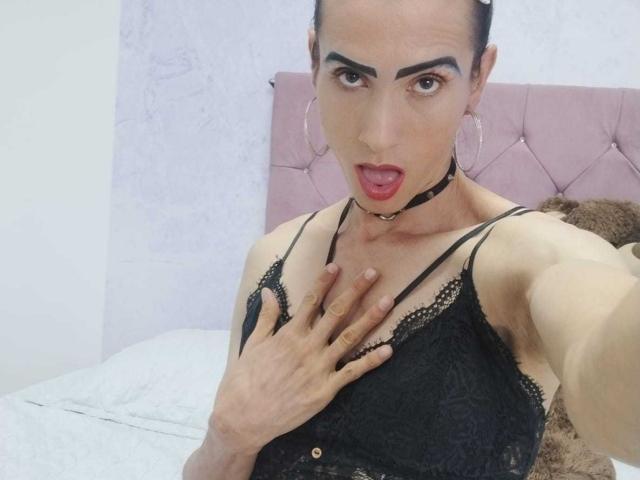 ShantalaNastasiia with dark hair, hoop earrings, black lace bra, and choker, hand on chest, mouth open, looking at camera, showing off her tits and cute face.