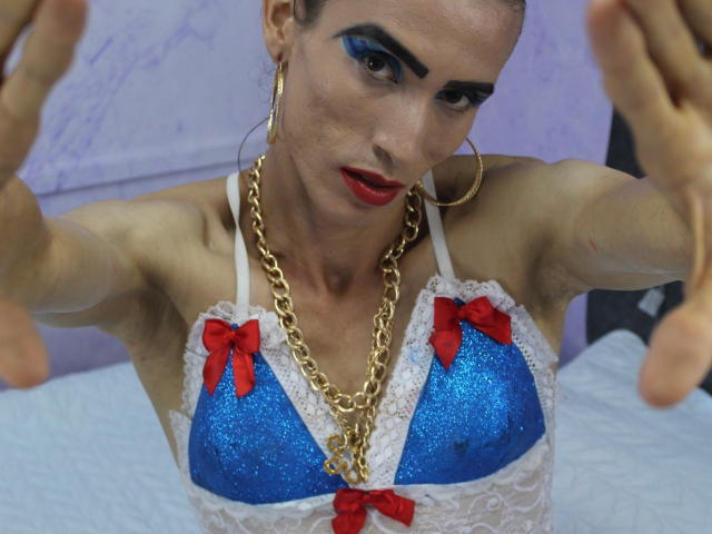 ShantalaNastasiia with blue glitter bra, red bows, lace, gold chain, hoop earrings, and red lipstick, arms raised, looking intense, dark blue eye makeup, pale skin, small tits.