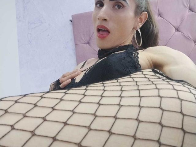 ShantalaNastasiia with her tits in a black lace bra, wearing fishnet, lying back on a pink tufted headboard, looking at the camera with her mouth slightly open.