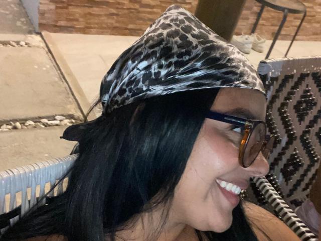 AmarantaCarey with black hair, wearing a leopard print bandana and glasses, smiling with visible teeth, has a cute face and is looking to the right.