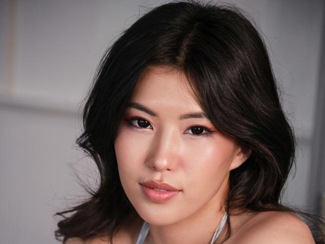 WendyFire has smooth, tan skin, dark wavy hair, and pinkish-brown eyes with subtle makeup. Her small, cute nose and full, pink lips are visible. She's wearing a gray halter.