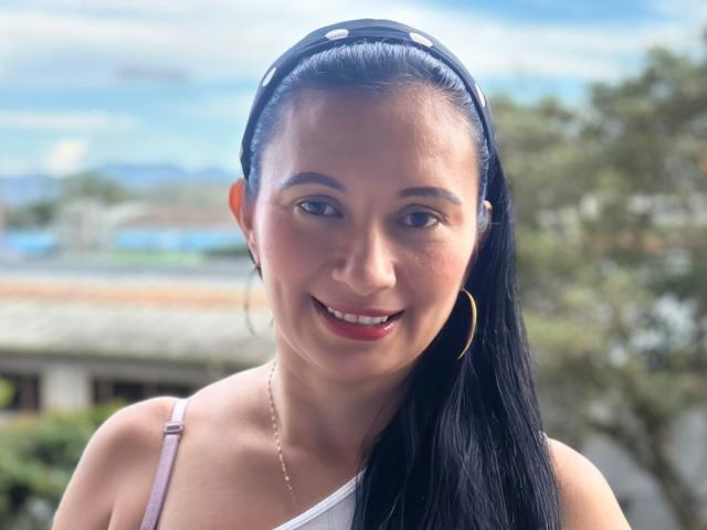 GraceK has dark black hair in a headband, smiling with red lips, wearing a white strap, gold hoop earrings, and a thin necklace, showing her cute face.