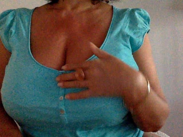 DeesseBleue's large tits in a tight, blue, button-up top with puffy sleeves. Her hand, with a gold ring, covers her chest. She has a silver bracelet.