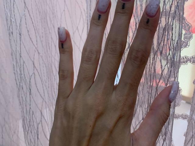 MoonLiza's hand with pale pink, glittery nails and small black dots on each nail, against a lace curtain. Her fingers are slightly spread, showing her delicate, manicured nails.