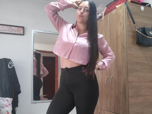 VenusSweetPalmer with long dark hair, pink button-up shirt, black high-waisted pants, pouting, hand on head, mirror reflection showing her ass, wooden closet, black bag on top.