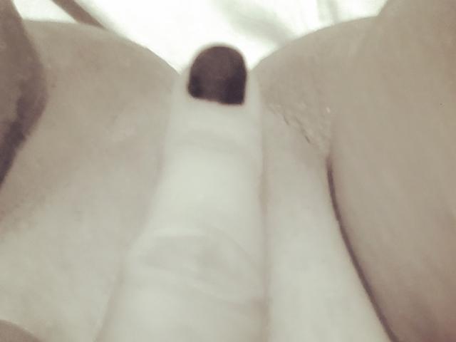 A vulva de MeahBrunette, com um objeto cilíndrico branco parcialmente inserido entre seus lábios ligeiramente separados. Sua pele é clara e a imagem é um close-up, ligeiramente desfocado..