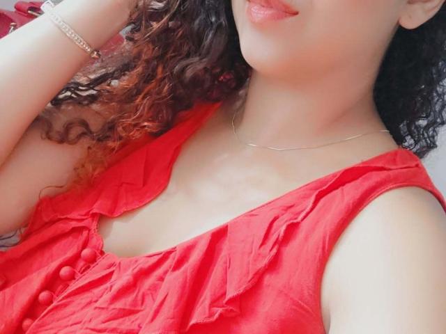 AleWalker's face and chest, showing curly brown hair, red dress with buttons, and a silver necklace. She's wearing a bracelet, with her tongue slightly out.