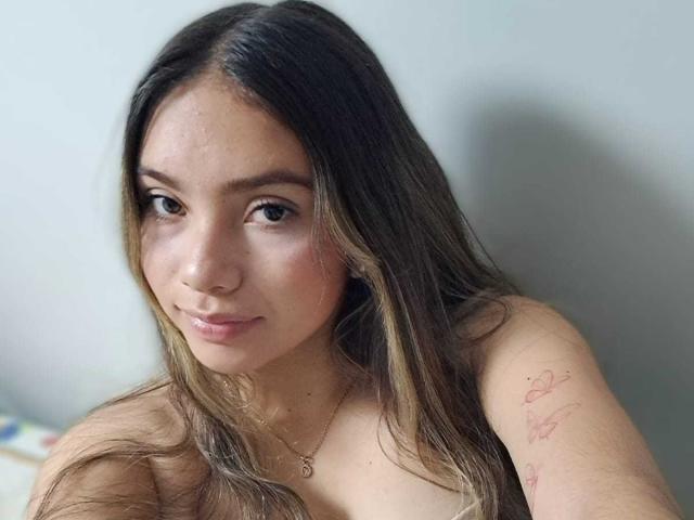 ValeryThomss with long brown hair, slight smile, and small nose ring, topless showing a tattoo on her right shoulder, and a necklace with a small pendant.