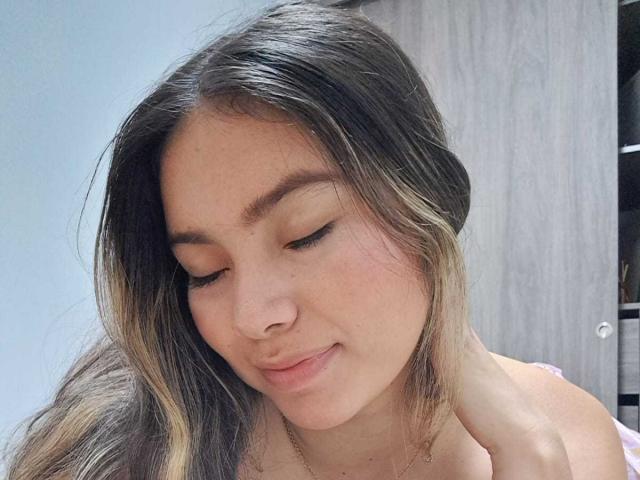 ValeryThomss has light brown skin, long brown hair with blonde highlights, and is looking down with a slight smile. Her eyes are closed, and she's wearing a pink top.