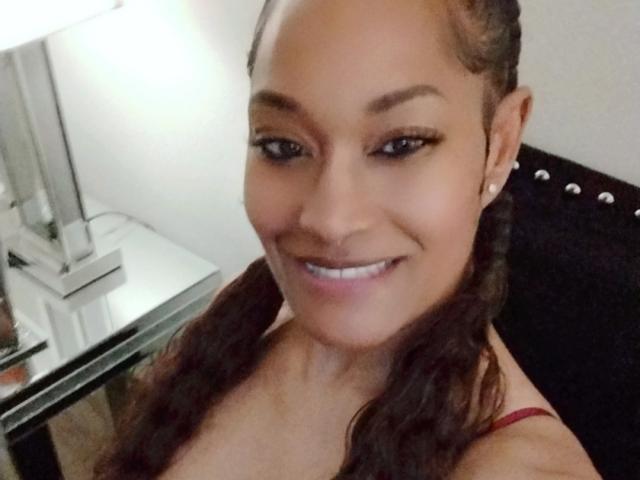 CarmelDelightF has brown skin, long wavy hair in pigtails, small earrings, and is smiling with white teeth, wearing a red strap, looking cute and sexy.