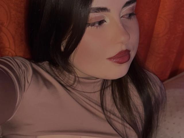 VicluX a de longs cheveux noirs, du fard à paupières rose et du rouge à lèvres rouge. Elle porte un haut transparent rose, et ses seins sont légèrement visibles. Un rideau rouge est visible en arrière-plan..