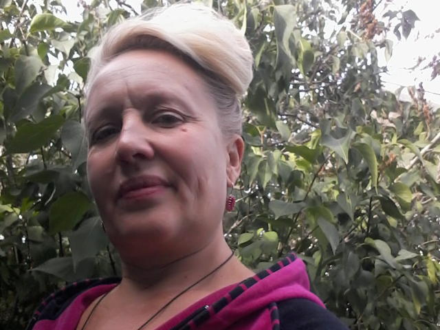 CerdAyaz has pale skin, blonde updo, pink lips, small nose, and wears a pink and black hoodie. She's got red earrings and a slight smile.
