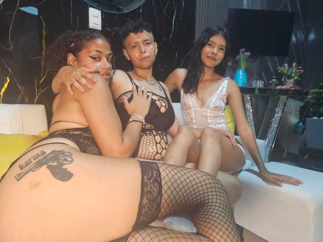 Three WomenThompson sitting on a white couch, wearing black and white lingerie, fishnet stockings, and showing tattoos. One has big ass, another has small tits, all have pretty pussy.