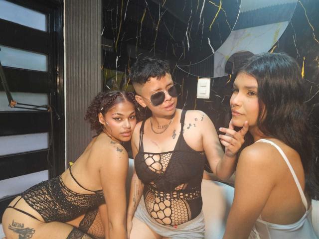 Three WomenThomson with tattoos, wearing black and white fishnet lingerie, standing together. WomanThomson on left has brown skin and curly hair, middle WomanThomson has short black hair and sunglasses.