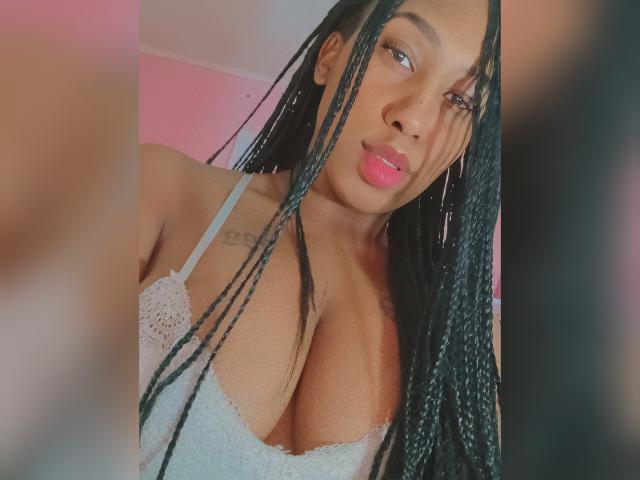EllenFantasy with long black braids, pink lips, and hoop earrings, wearing a white lace bra that shows her big tits. Her brown skin is smooth, and she's looking at the camera.