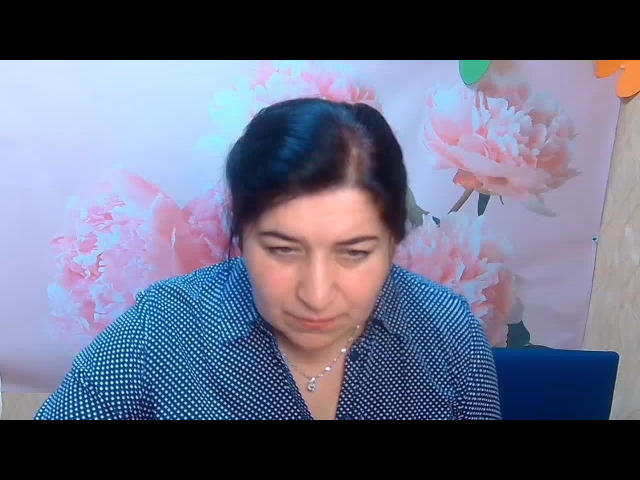 BridjetTur with dark hair, wearing a blue polka dot shirt, has a small, round ass and a slight, shy smile, looking downward with a subtle, gentle expression.