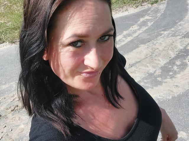 SensualNathalie has black shoulder-length hair, green eyes, and is pouting her lips slightly. She's wearing a black top, and her small tits are subtly visible.