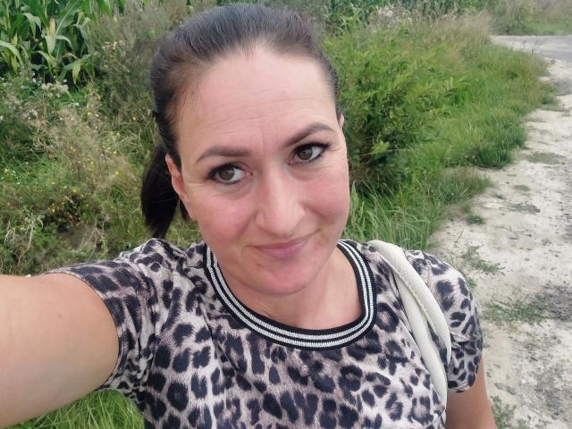 SensualNathalie has a cute smile, brown eyes, and wears a leopard print shirt. She's holding a selfie with grass and a dirt path in the background.