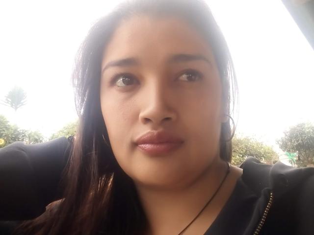 ZafiRouge has medium brown skin, dark brown eyes, and glossy pink lips. She's wearing a black hoodie with a zipper, and has long dark brown hair.