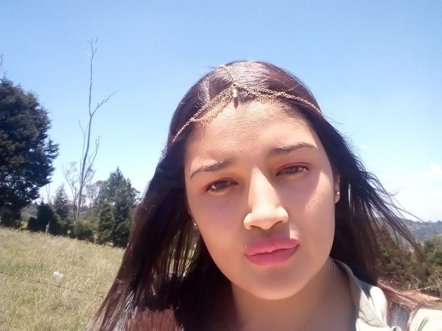 ZafiRouge's face with brown hair, gold head chain, pink lipstick, and light skin. She's looking at the camera with a neutral expression. Her tits aren't visible.