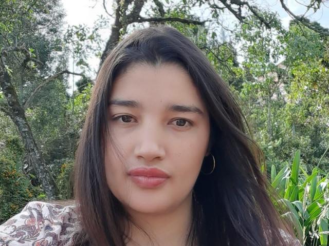 ZafiRouge has long dark brown hair, brown eyes, and pinkish lips. She's wearing a patterned shirt with a gold hoop earring. Her face is centered, looking at the camera.