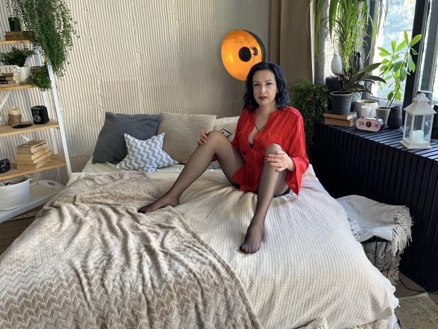 ElizabethSo, sitting on a bed, wearing a red shirt, black sheer pantyhose, exposing her pussy, with black hair, fair skin, and a sexy smile, in a cozy room.