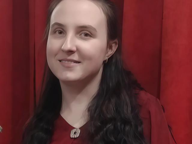 CatherineNelson with pale skin, brown eyes, long black wavy hair, red dress, small gold earrings, slight smile, and a bald spot on the right side of her head.