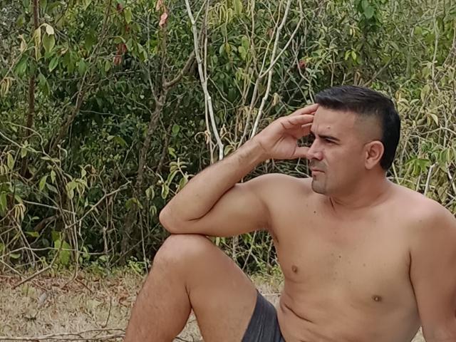 WolfineOne is a shirtless, muscular dude with a slightly hairy chest, short black hair, and gray shorts, sitting with one hand on his forehead, looking annoyed.