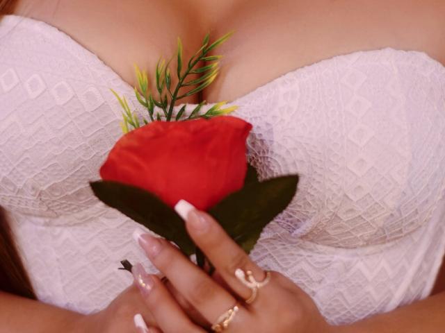 KylieCharm holding a red rose with green leaves, her white lace bra covering her tits, wearing gold rings and nail polish with a French tip.