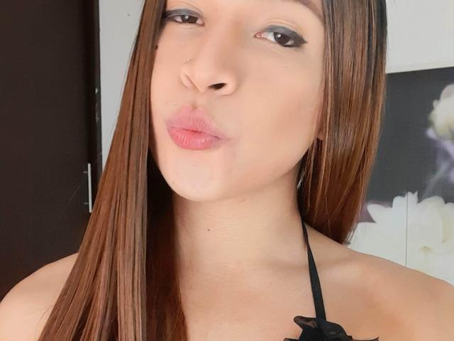 SanzJulie's pouty face with brown hair, light skin, and pink lips, wearing a black halter top, has a small nose piercing and subtle eyeliner.