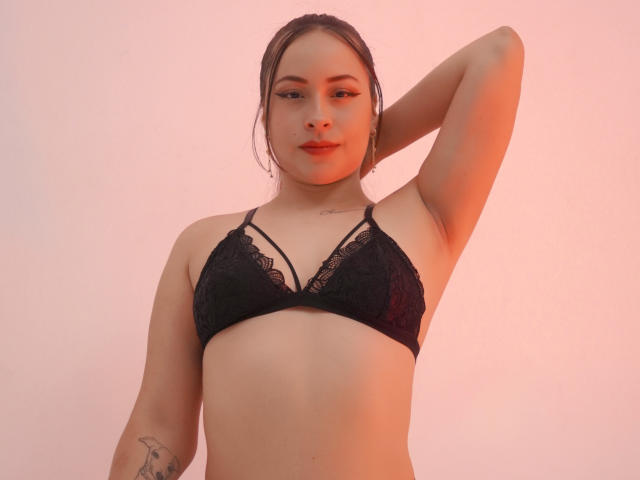 ValeriaJames with her arm raised, wearing a black lace bra, showing her small tits and a tattoo on her right arm. She has a cute face and light skin.
