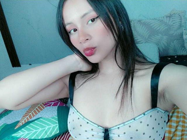 TinyLaurent has light skin, black hair, and pouty pink lips, wearing a sheer polka dot bra, showing her small boobs, and resting her head on her hand.