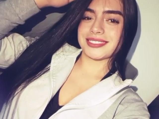EmaRosee with long black hair, smiling, wearing a gray hoodie, has a cute face, small nose, and is showing off her pearly white teeth. She's looking cute and sexy.