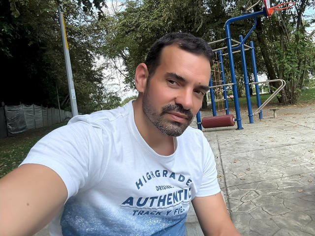 XRawForU has a medium build, short dark hair, and a stubble. He's wearing a white "Higrade" t-shirt with "Autenthic" text. His ass is partially visible.