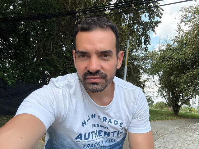 XRawForU is a middle-aged dude with a short beard and gray hair, wearing a white shirt, looking into the camera with a serious expression. His ass is not visible.