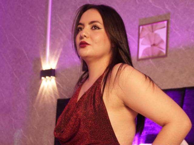 ValeriJoness with long black hair, red glitter dress, showing sideboob, purple light, and red lipstick, looking confident, slightly pouty.