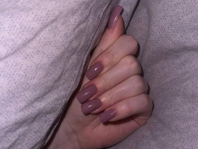 Barberry's hand with pinkish-purple, long, almond-shaped nails gripping a gray, textured fabric. Her fingers are slightly curled, showing smooth skin.