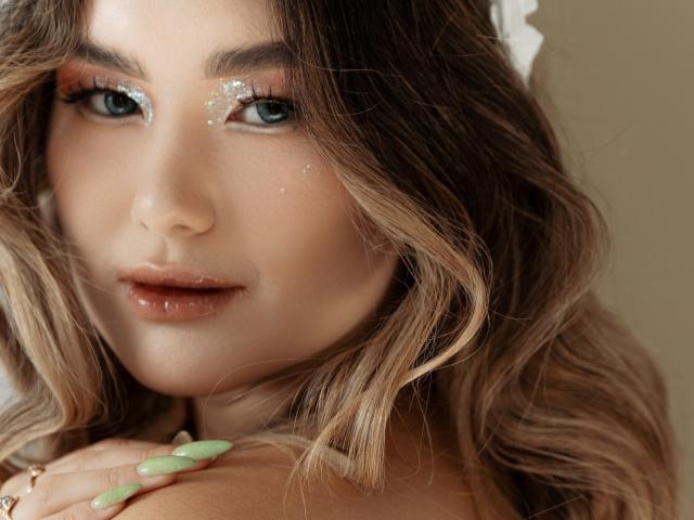 AnneTLuis has blue eyes, wavy brown hair, sparkly eyeshadow, and green nails with a sexy, slightly parted lip look. Her tan skin and soft makeup are hot.