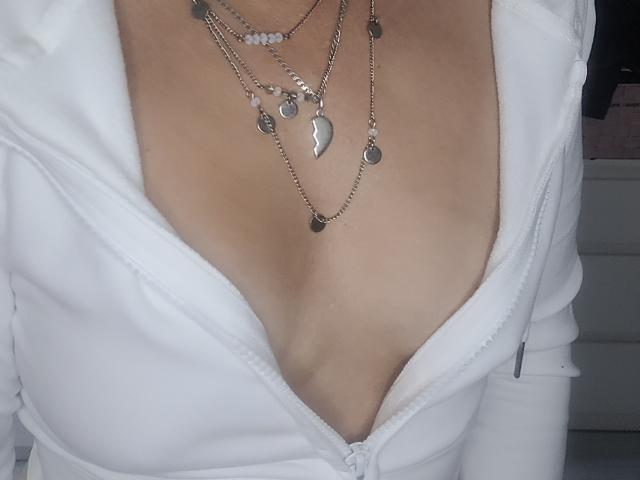 ElylaFrenchy's tits, visible through a deep V-neck white zip-up, are adorned with multiple silver chain necklaces featuring heart and circular pendants. Her skin is light.