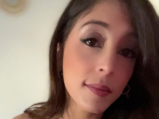 Lolita123456 has medium brown skin, dark brown hair, black eyeliner, and pink lipstick. She's smiling with a slight tilt of her head, wearing small hoop earrings.