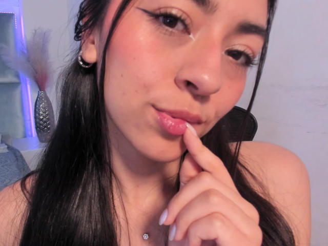 CanelleGarces has a cute face with black hair, pink pouty lips, and a finger touching her bottom lip. She has a nose ring and a small piercing above her tits.
