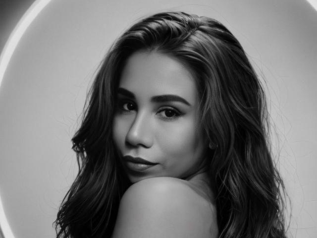 LunaMiranda has wavy dark hair, full eyebrows, and a seductive look, with her shoulder and ear visible, in a black-and-white portrait. Her lips are slightly parted.