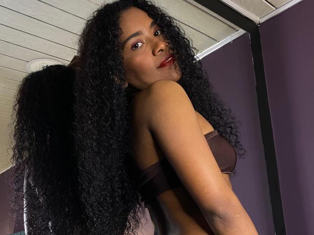 KendalBoston with curly black hair, dark brown strapless top, looking over shoulder, red lipstick, showing bare back, small black wings on right.