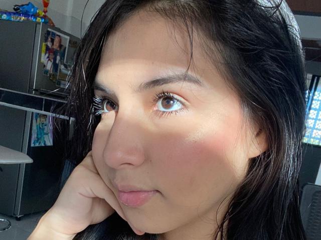 CristalDolce's face, brown eyes, light brown skin, black hair, slight blush on cheeks, hand under chin, soft smile, sunlight highlighting face.