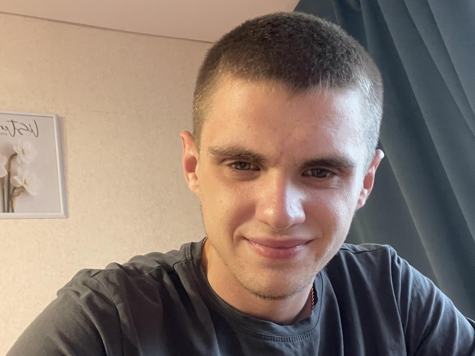 JamesGreens has short brown hair, a slight smile, and is wearing a gray shirt. He has light skin, brown eyes, and a small goatee. His nose is slightly upturned.