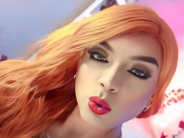 KarolElegance has orange hair, full red lips, and dark eyeliner. Her pale skin and serious expression make her look sexy. Her small nose and slightly parted lips are prominent.