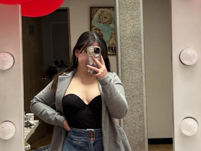 VicluX with long dark hair, wearing a gray cardigan over a black strapless bustier, showing her tits, holding a phone in front of a mirror.