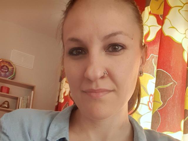 Swissmiss88-hot has a nose piercing, light brown eyes, and a slight smile. She's wearing a blue shirt with her brown hair tied back.