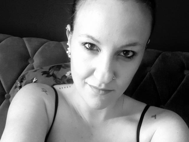 Swissmiss88-hot, black-and-white selfie, showing a nose ring, small tattoos on shoulder, and upper chest, with a slight smile, wearing a black spaghetti strap top, looking at camera.